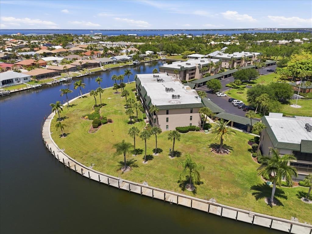 An aerial view shows a multi-story apartment building surrounded by a lawn and a canal — 601 SHREVE STREET UNIT 32B, PUNTA GORDA, FL
