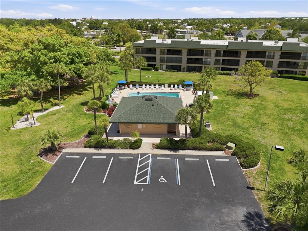 An aerial view shows a community swimming pool, clubhouse, and parking lot near an apartment building — 601 SHREVE STREET UNIT 32B, PUNTA GORDA, FL