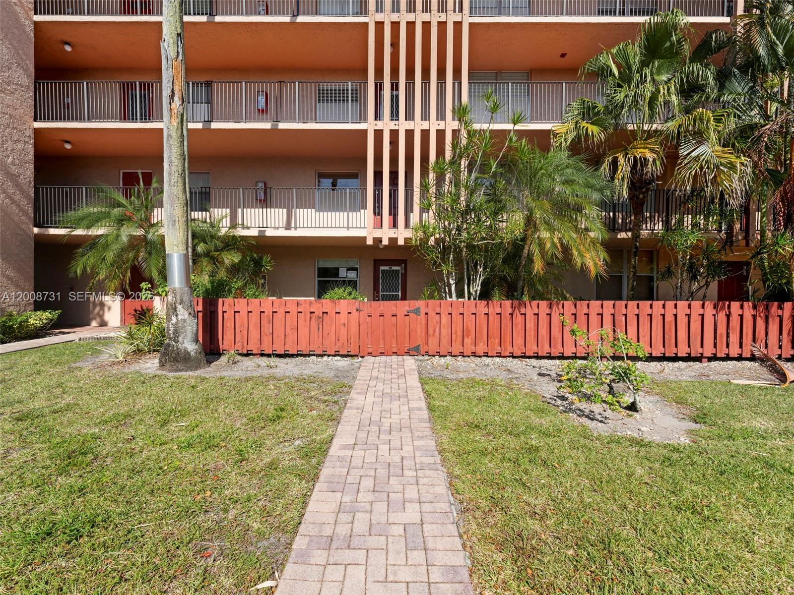 A brick walkway leads to a fenced ground-floor apartment entrance at a multi-story building — 480 NW 76th Ave # 102, Margate FL 33063, MARGATE, FL