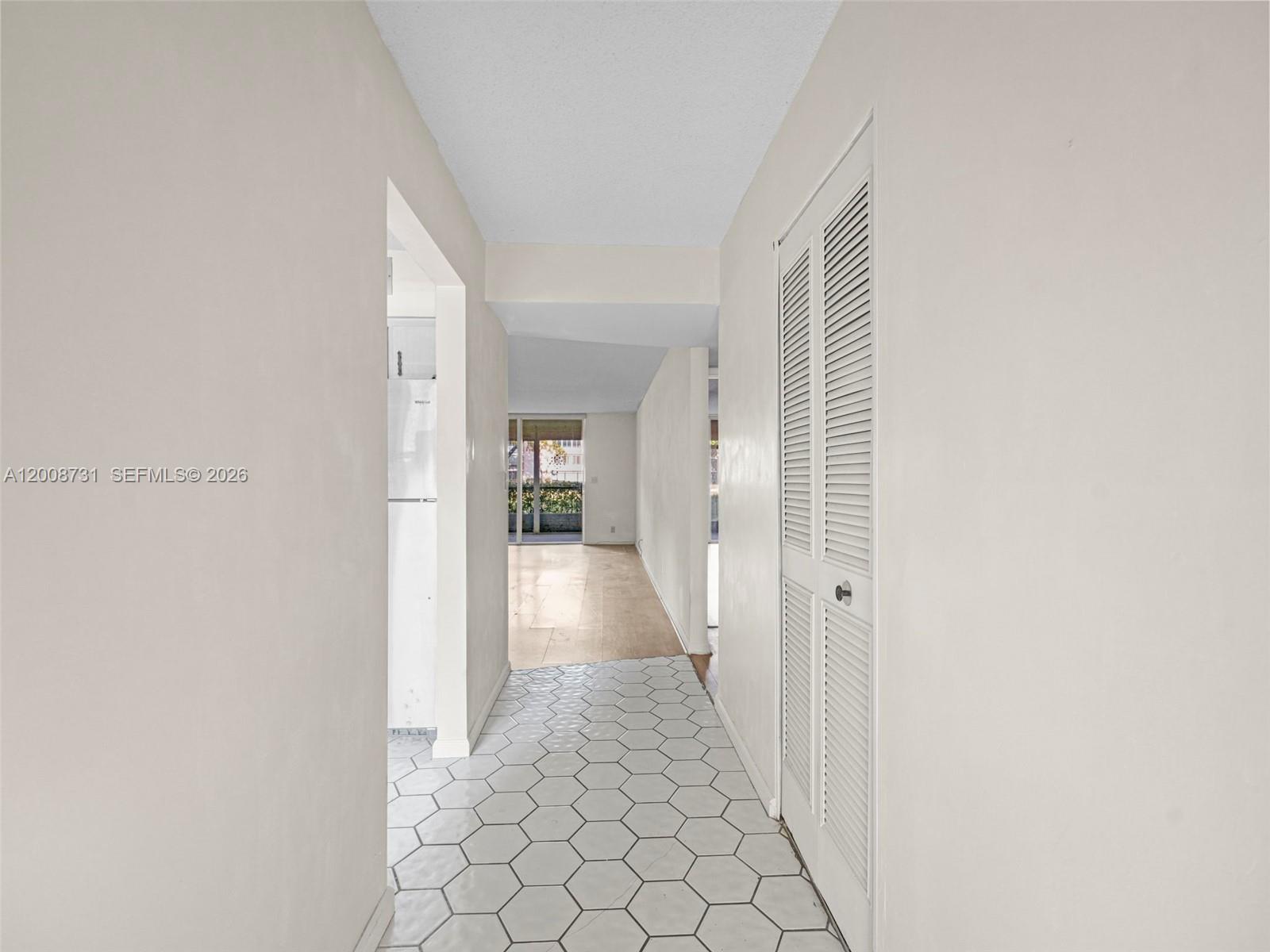 A hallway with white hexagonal floor tiles leads toward a bright living area — 480 NW 76th Ave # 102, Margate FL 33063, MARGATE, FL