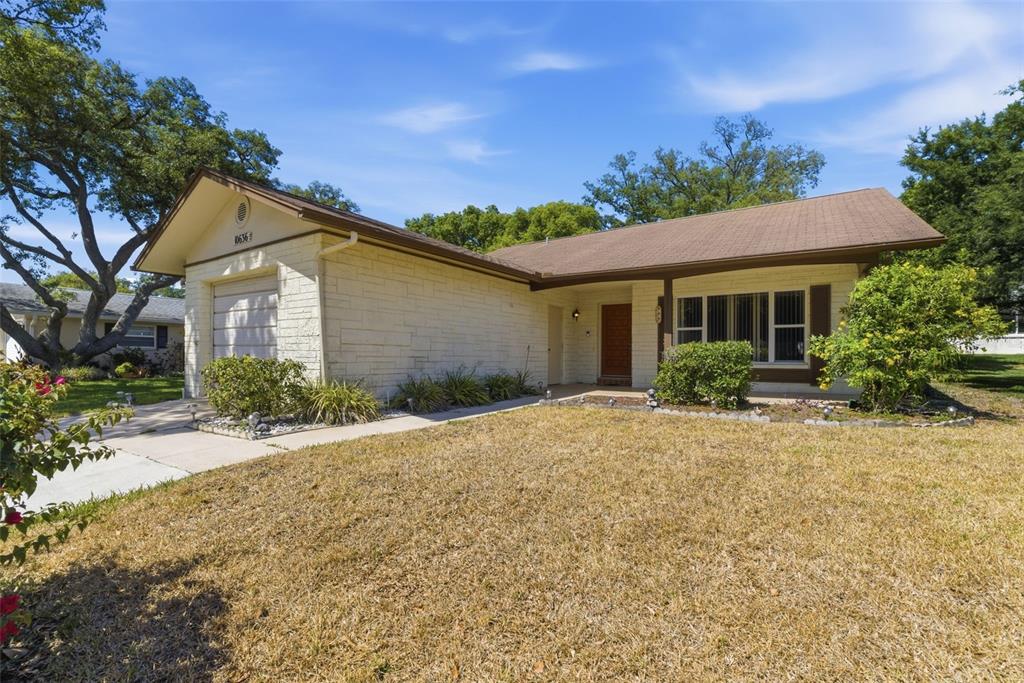 A single-story house with a light-colored stone facade and a brown shingled roof — 10636 SALAMANCA DRIVE, PORT RICHEY, FL