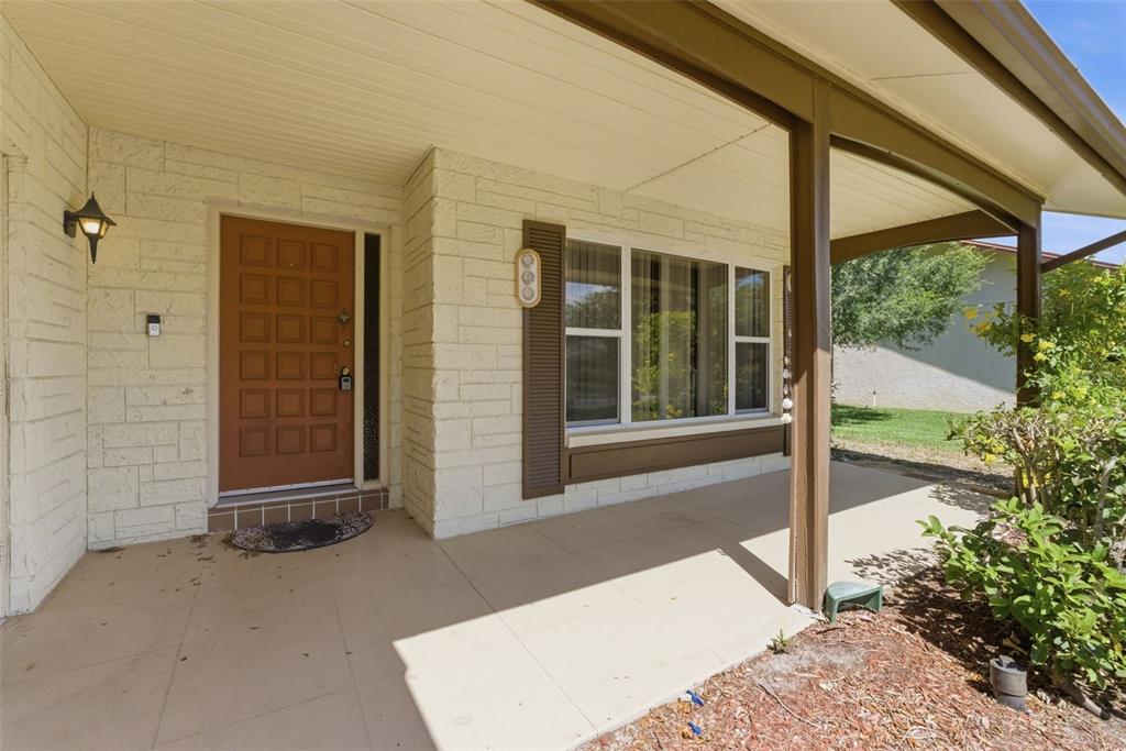 A covered front porch with a brown door, large window, and light-colored stone siding — 10636 SALAMANCA DRIVE, PORT RICHEY, FL