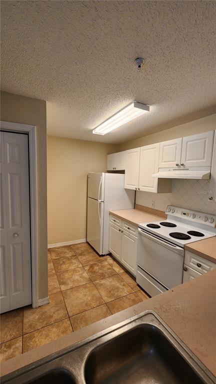 A kitchen features white cabinets, a white refrigerator, a white stove, and brown tile flooring — 18001 RICHMOND PLACE DRIVE UNIT 1033, TAMPA, FL