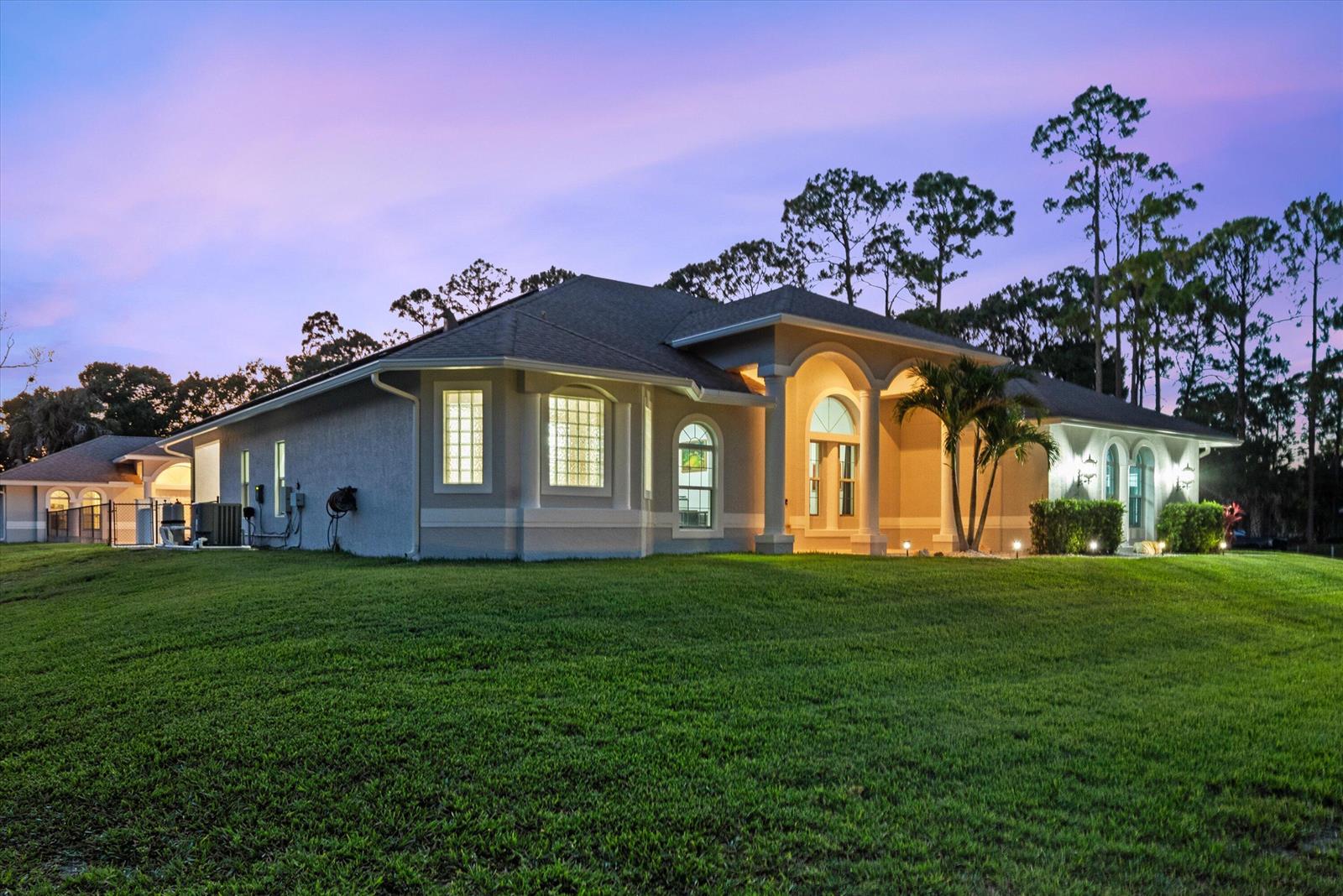 A single-story house with a stucco exterior, arched entryway, and glass block windows at dusk — 17038 N 61st Pl Place N, FL 33470, FL