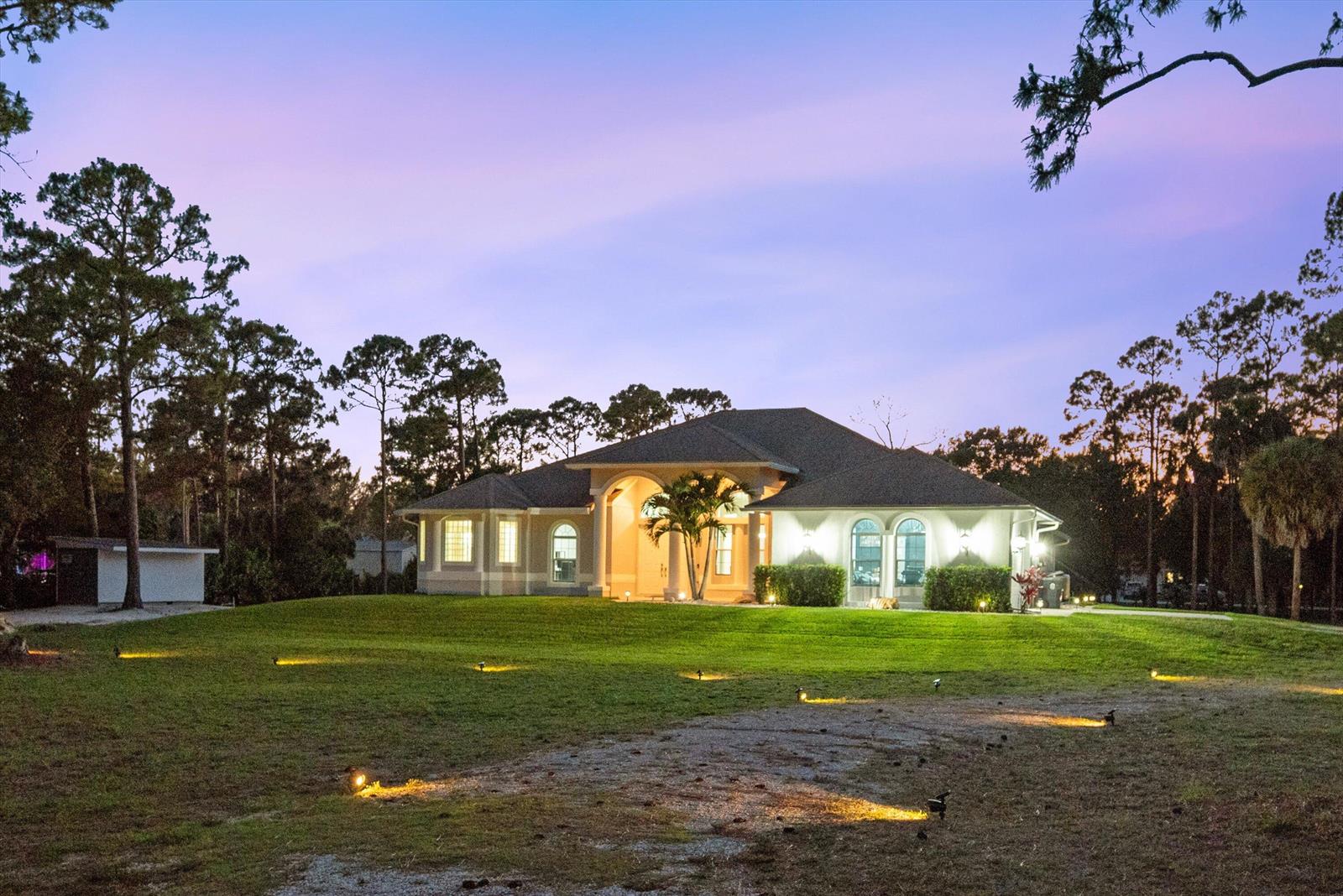 A single-story house with a large lawn and exterior landscape lighting at dusk — 17038 N 61st Pl Place N, FL 33470, FL