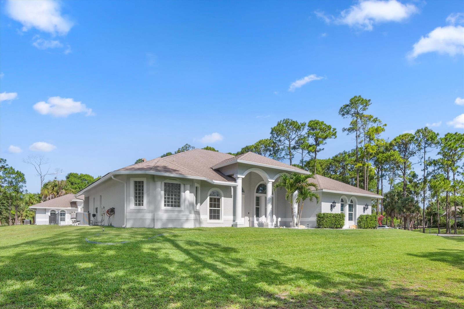 A single-story house with a light-colored exterior, arched entryway, and a large grassy yard — 17038 N 61st Pl Place N, FL 33470, FL