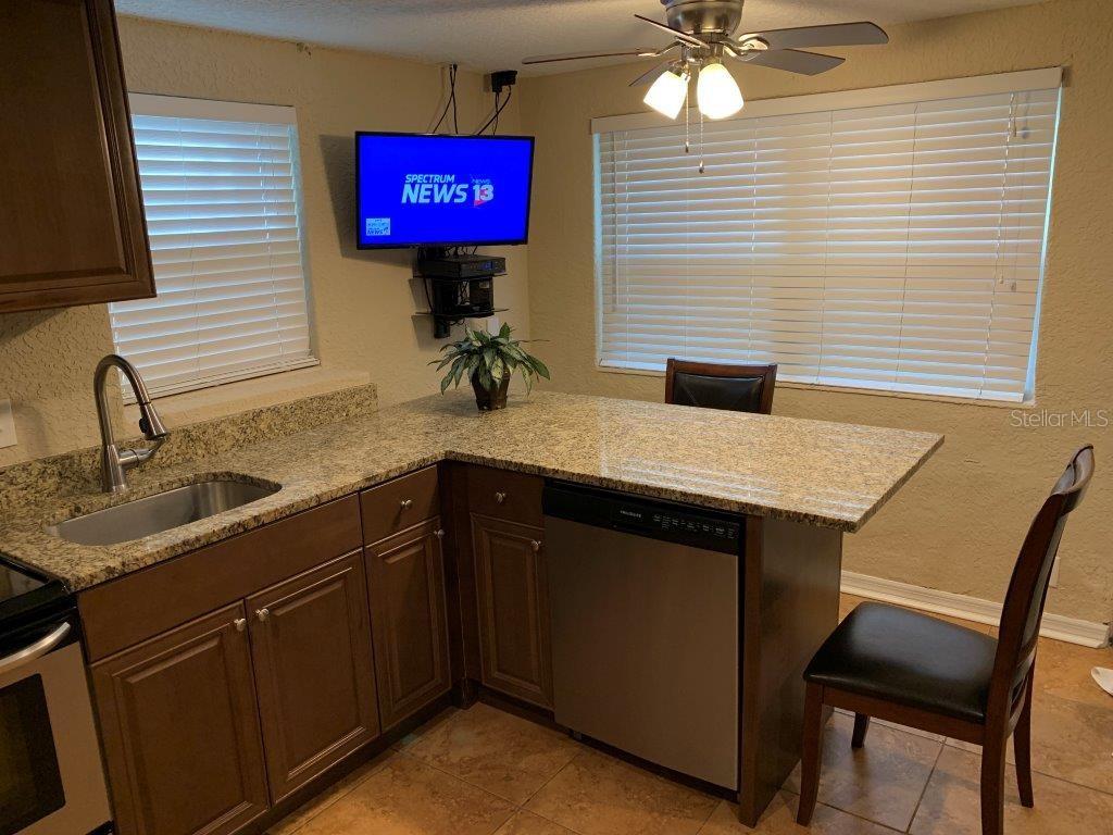A kitchen features brown cabinets, granite countertops, a stainless steel dishwasher, and a wall-mounted television — 2512 MUSSELWHITE AVENUE UNIT 3, ORLANDO, FL