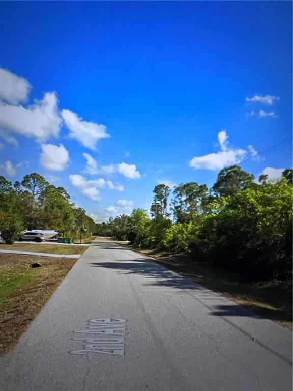 A paved road stretches into the distance, flanked by trees and a residential property — 11491 2ND AVENUE, PUNTA GORDA, FL