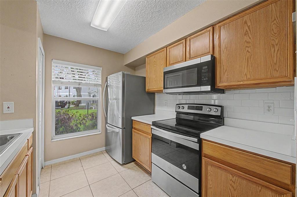 A kitchen features wood cabinets, stainless steel appliances, white subway tile backsplash, and a window — 7434 E BANK DRIVE, TAMPA, FL