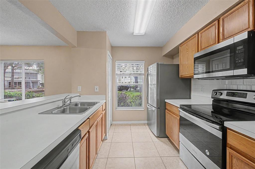 A kitchen features light wood cabinets, stainless steel appliances, a double sink, and tile flooring — 7434 E BANK DRIVE, TAMPA, FL