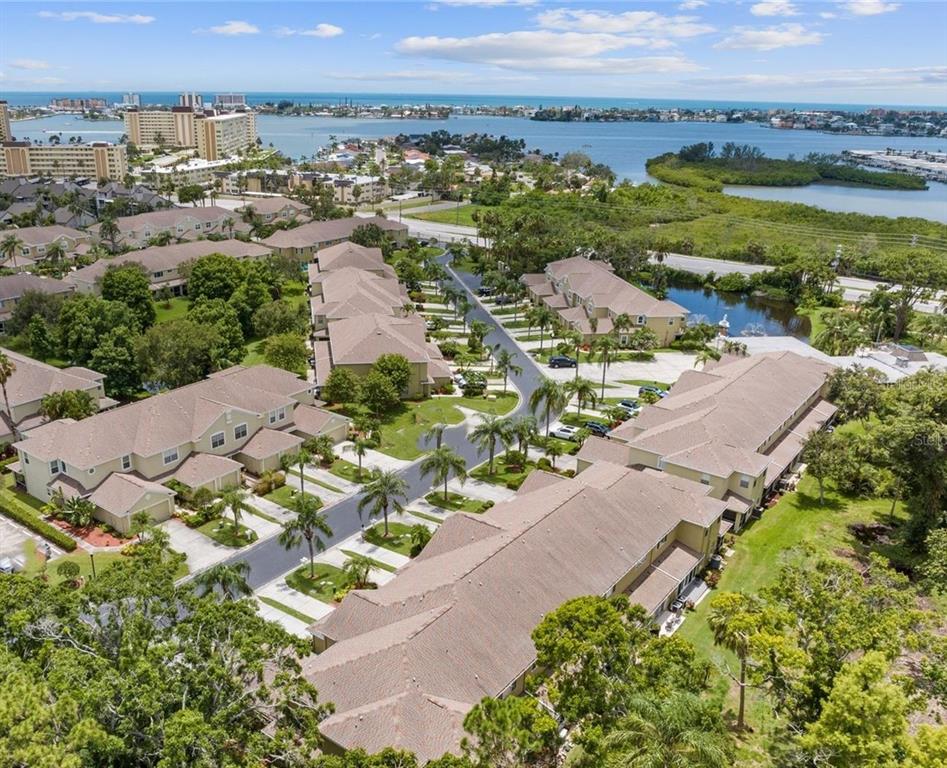 An aerial view of a residential complex with multiple buildings, palm trees, and nearby water — 11235 KAPOK GRAND CIRCLE, MADEIRA BEACH, FL