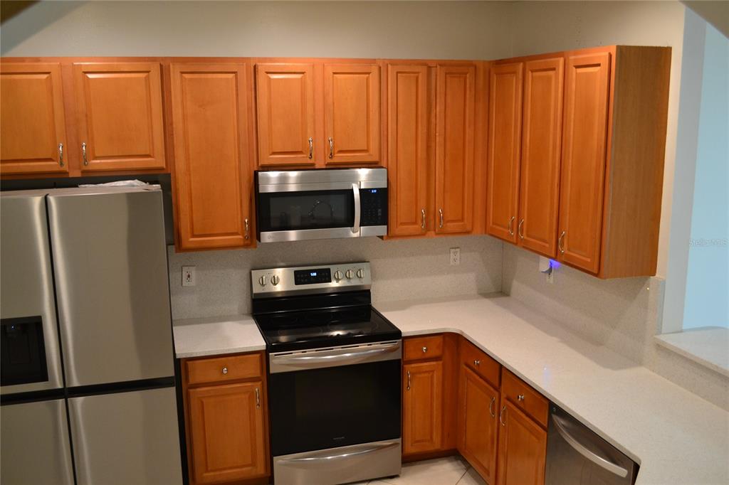 A kitchen featuring wood cabinets, stainless steel appliances, and light-colored countertops — 11235 KAPOK GRAND CIRCLE, MADEIRA BEACH, FL