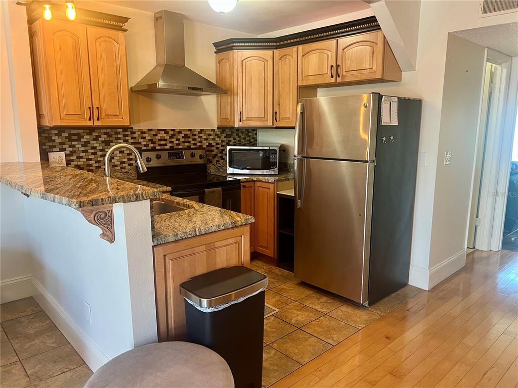 A kitchen features wood cabinets, granite countertops, stainless steel appliances, and a tile backsplash — 24862 US HIGHWAY 19 N UNIT 1804, CLEARWATER, FL