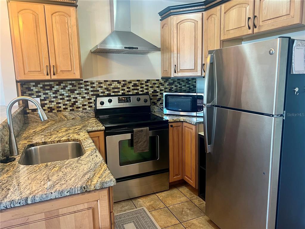 A kitchen features light wood cabinets, granite countertops, stainless steel appliances, and a mosaic backsplash — 24862 US HIGHWAY 19 N UNIT 1804, CLEARWATER, FL