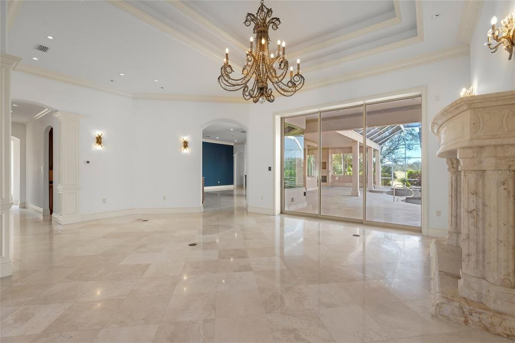 A spacious living room features marble floors, a large chandelier, and sliding glass patio doors — 6702 CHANCERY PLACE, UNIVERSITY PARK, FL