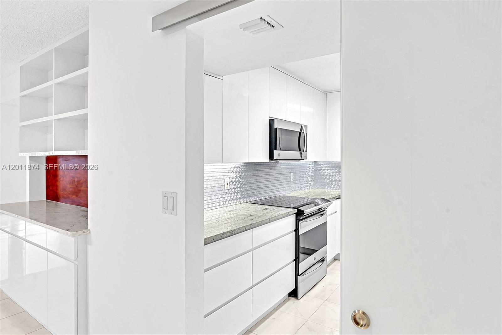 A galley kitchen features white cabinets, stainless steel appliances, and a metallic tiled backsplash — 2500 Parkview Dr # 1219, Hallandale Beach FL 33009, HALLANDALE BEACH, FL