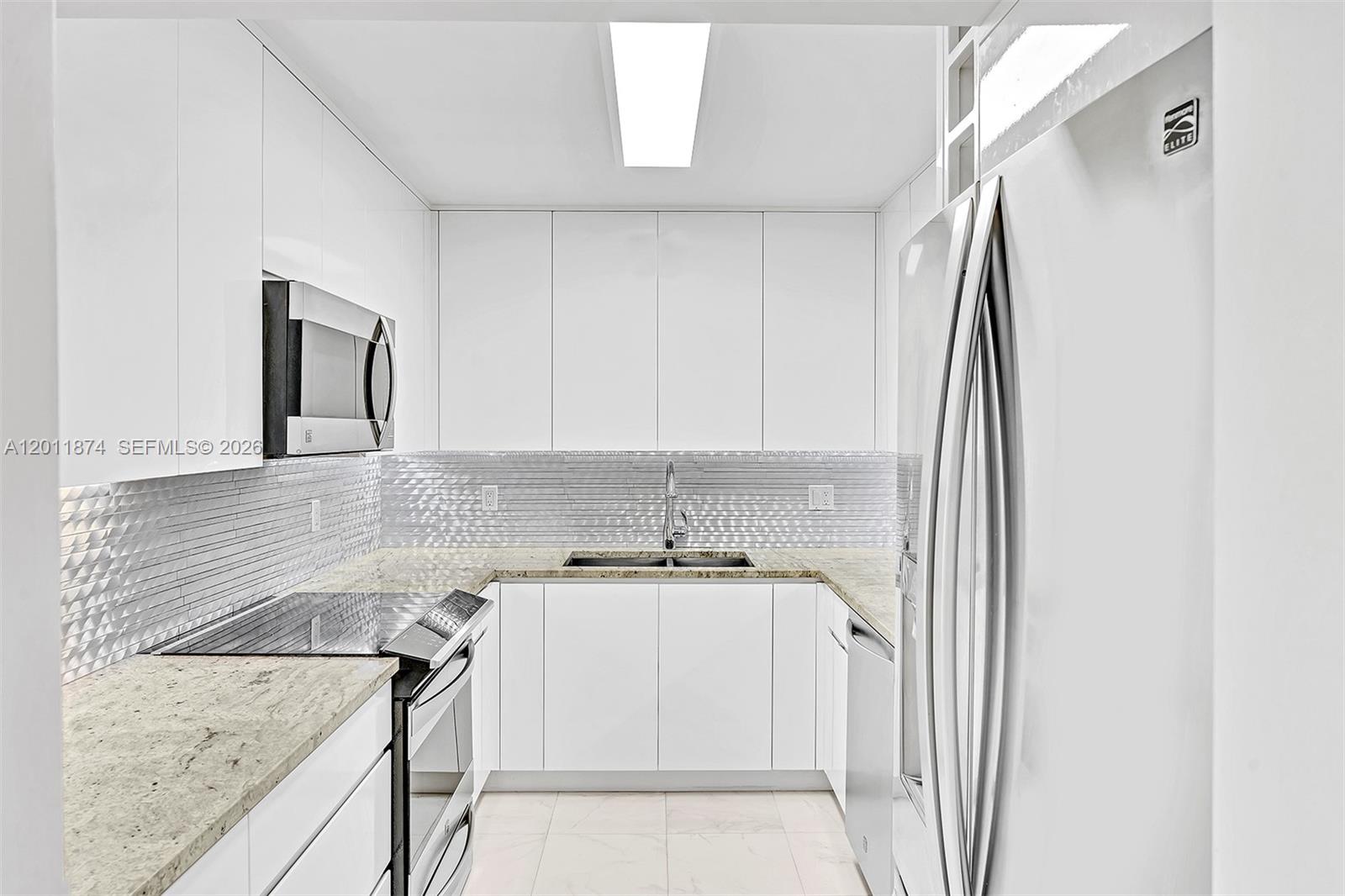 A galley kitchen features white cabinets, stainless steel appliances, and a textured metallic backsplash — 2500 Parkview Dr # 1219, Hallandale Beach FL 33009, HALLANDALE BEACH, FL