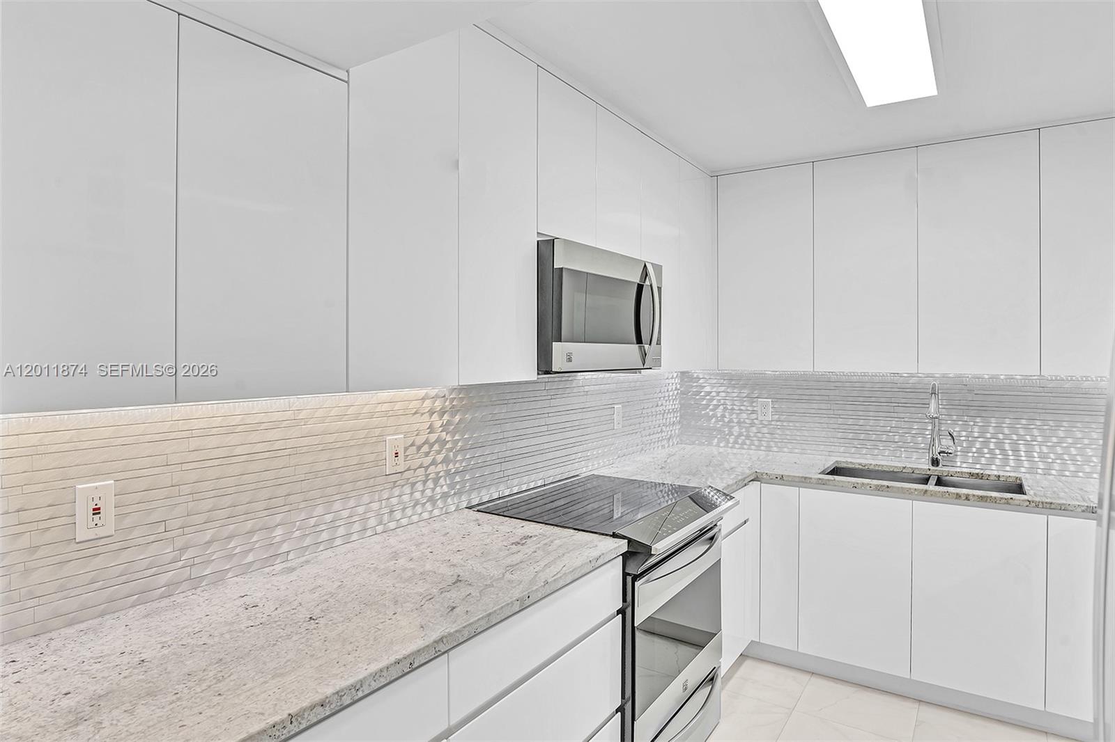 A modern kitchen features white flat-panel cabinets, granite countertops, and a textured tile backsplash — 2500 Parkview Dr # 1219, Hallandale Beach FL 33009, HALLANDALE BEACH, FL