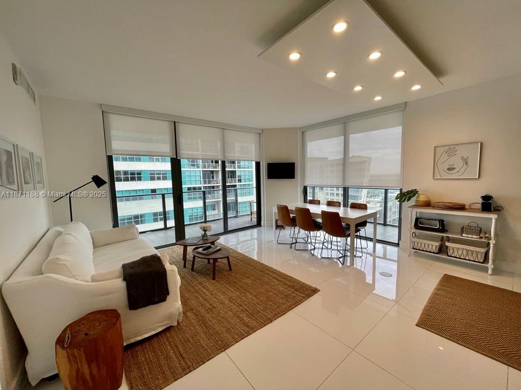 A modern living and dining area features white tile floors, large windows, and neutral furniture — 121 NE 34 ST # 901, Miami FL 33137, MIAMI, FL