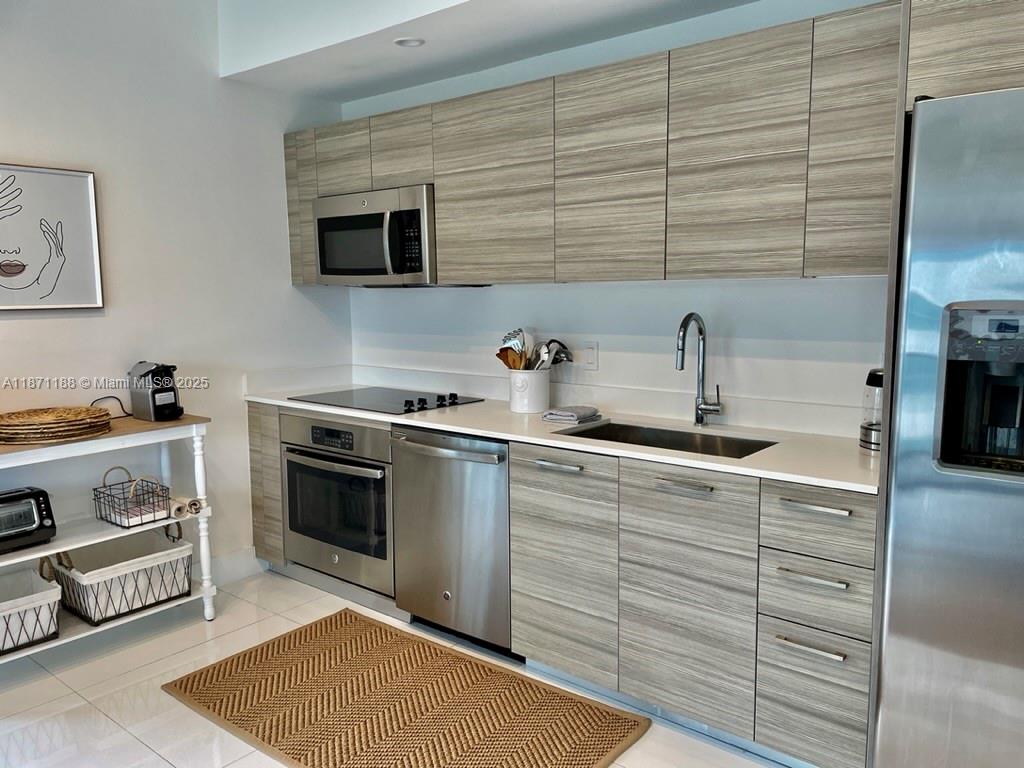 A modern kitchen features wood-grain cabinets, stainless steel appliances, and white countertops — 121 NE 34 ST # 901, Miami FL 33137, MIAMI, FL