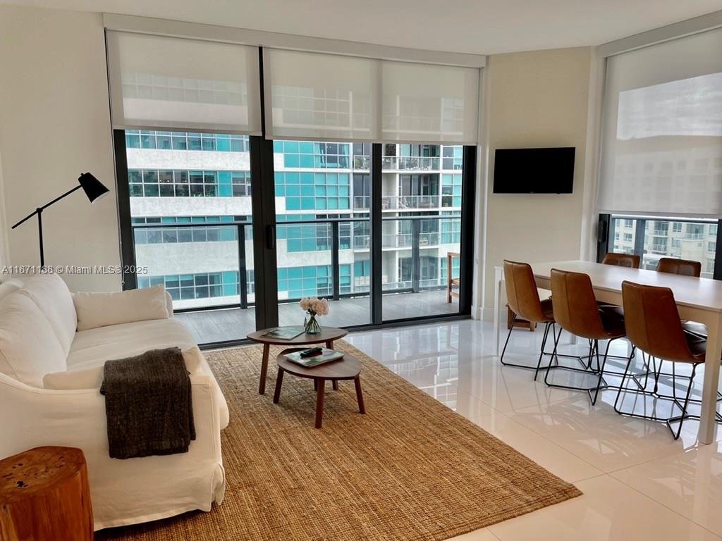 A modern living and dining area features white tile floors, floor-to-ceiling windows, and a balcony — 121 NE 34 ST # 901, Miami FL 33137, MIAMI, FL