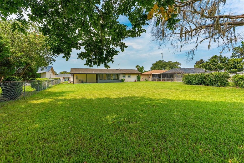 A wide, grassy backyard features a single-story house with a screened-in patio under large trees — 2955 CARRIAGE DRIVE, SOUTH DAYTONA, FL