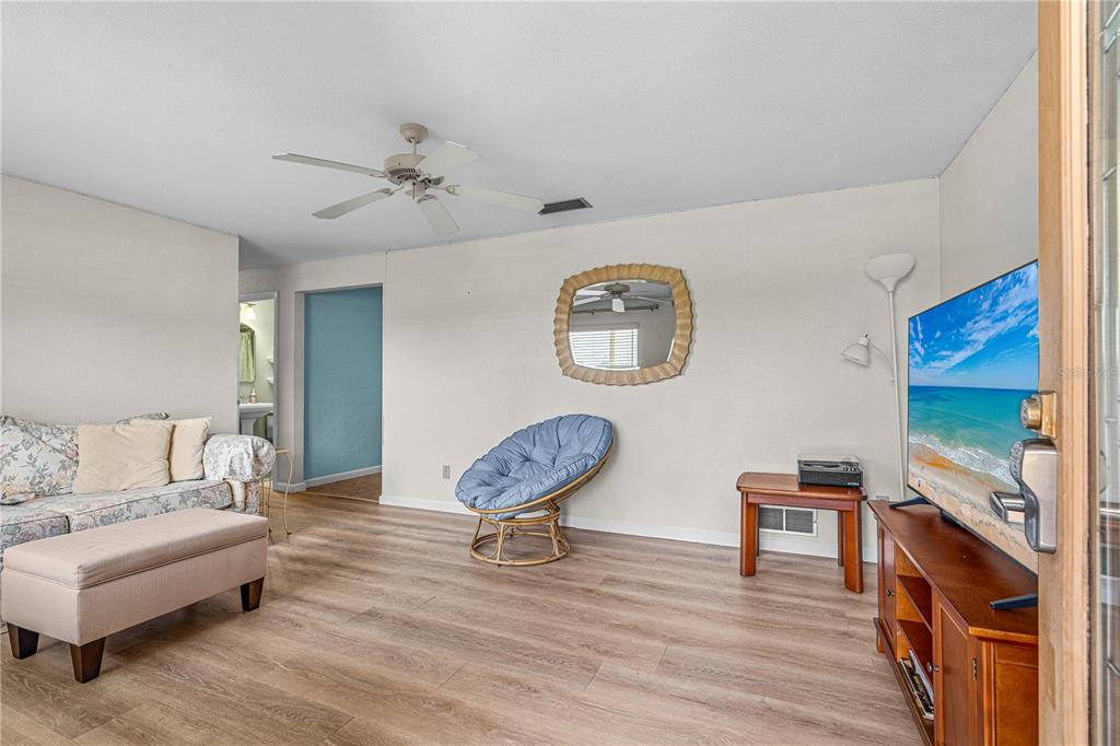 A living room features light wood-look flooring, a floral sofa, a blue chair, and television — 2955 CARRIAGE DRIVE, SOUTH DAYTONA, FL
