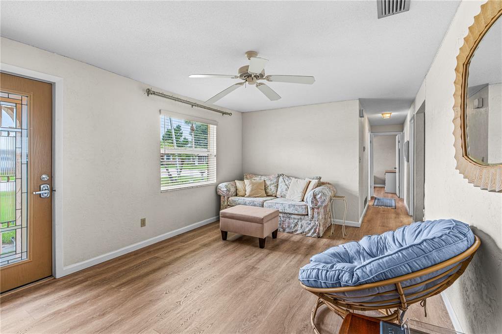 A living room features light wood-look flooring, a floral sofa, a blue papasan chair, and ceiling fan — 2955 CARRIAGE DRIVE, SOUTH DAYTONA, FL