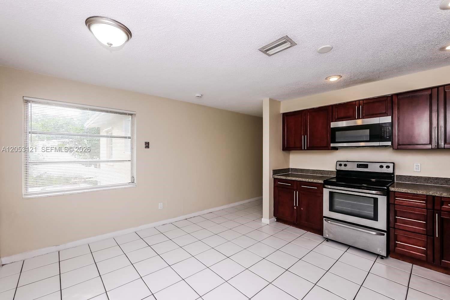 A kitchen features dark wood cabinets, stainless steel appliances, and white tiled flooring — COOPER CITY, FL