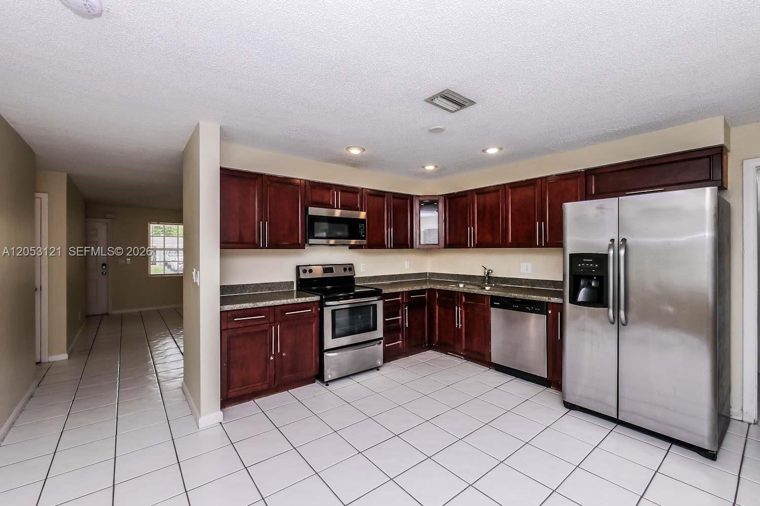 A kitchen features dark wood cabinets, stainless steel appliances, and white tile flooring — COOPER CITY, FL