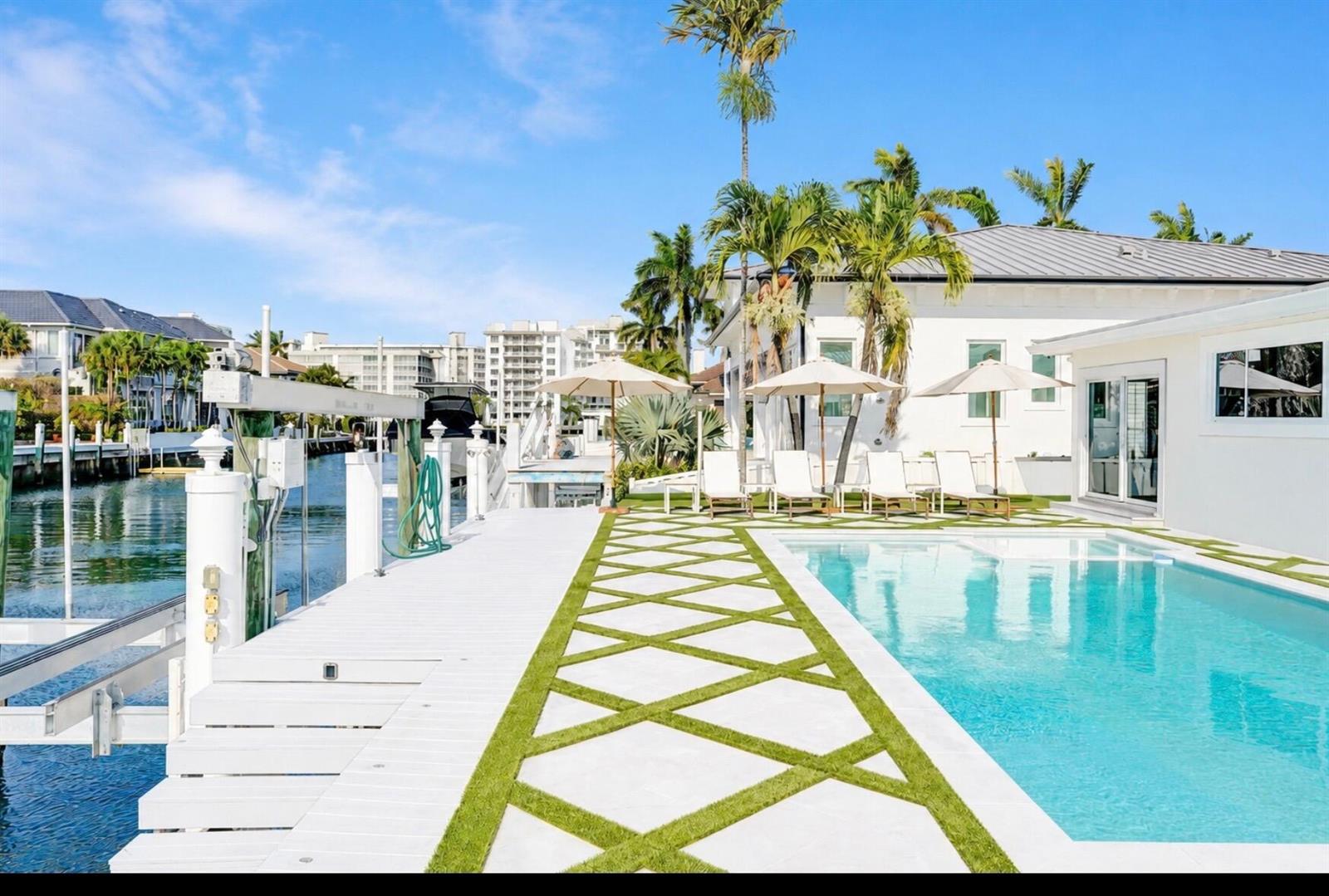A swimming pool and white deck with a geometric grass pattern sit beside a canal — 885 Nafa Drive, Boca Raton FL 33487, BOCA RATON, FL