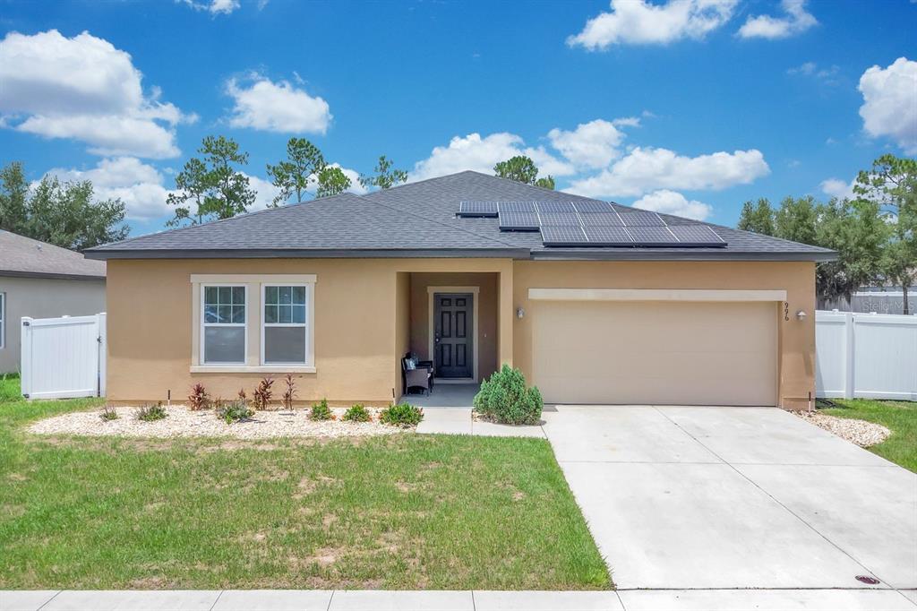 A single-story house with a tan stucco exterior, a two-car garage, and rooftop solar panels — 996 JOYCE ROAD, LAKE WALES, FL