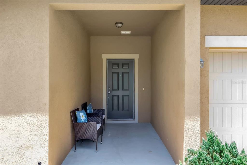 A covered entryway features a dark gray front door, two wicker chairs, and beige stucco walls — 996 JOYCE ROAD, LAKE WALES, FL