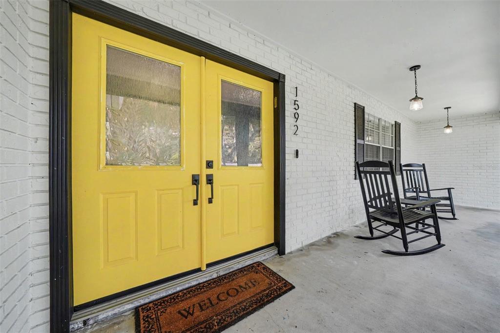 A bright yellow double front door sits on a porch with white brick and rockers — 1592 SKYLINE DRIVE, KISSIMMEE, FL