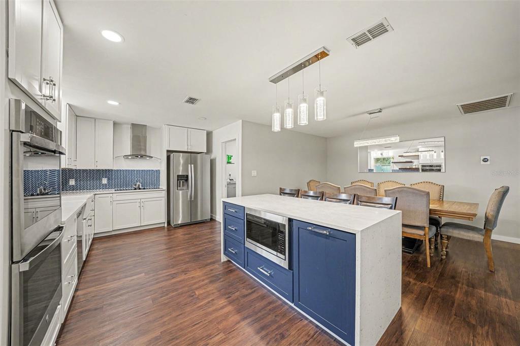A kitchen with white cabinets, a blue island, stainless steel appliances, and an adjacent dining area — 1592 SKYLINE DRIVE, KISSIMMEE, FL