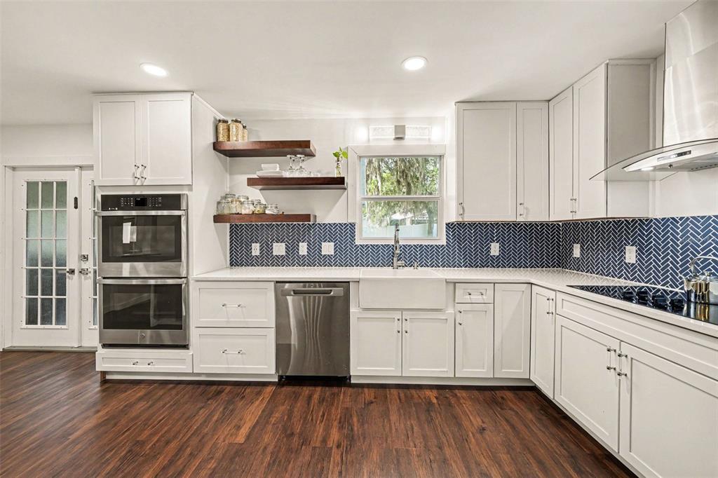 A kitchen features white cabinets, a blue herringbone backsplash, open wood shelving, and stainless appliances — 1592 SKYLINE DRIVE, KISSIMMEE, FL