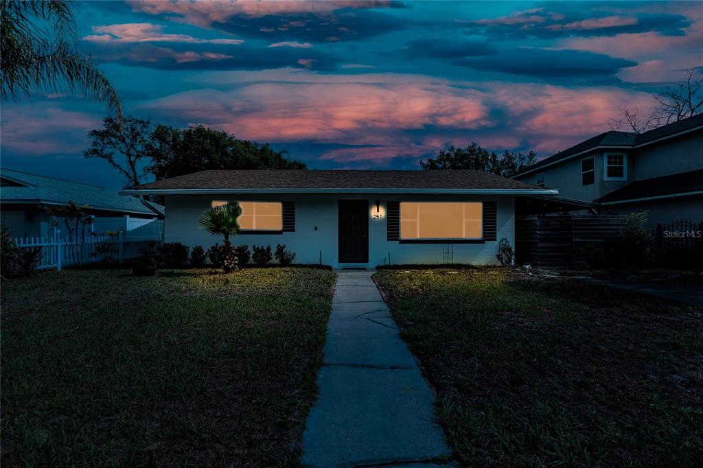 A single-story house with a white exterior and a front walkway at dusk — 251 PINE TREE DRIVE, CASSELBERRY, FL