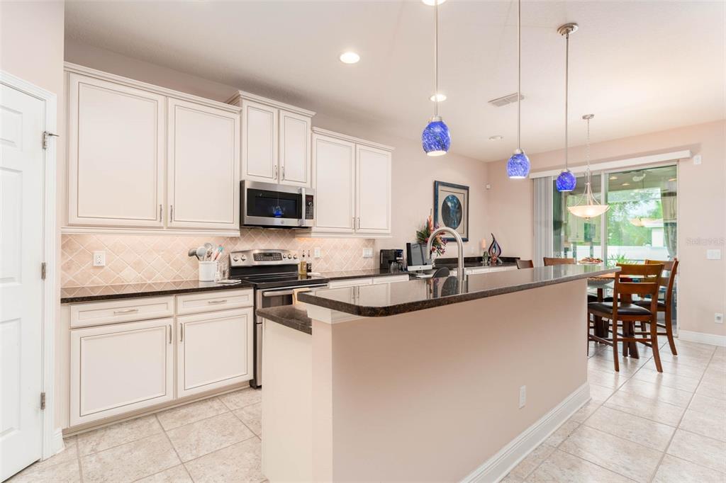 A kitchen features white cabinets, dark granite countertops, a breakfast bar, and three blue pendant lights — 220 PARSONS WOODS DRIVE, SEFFNER, FL