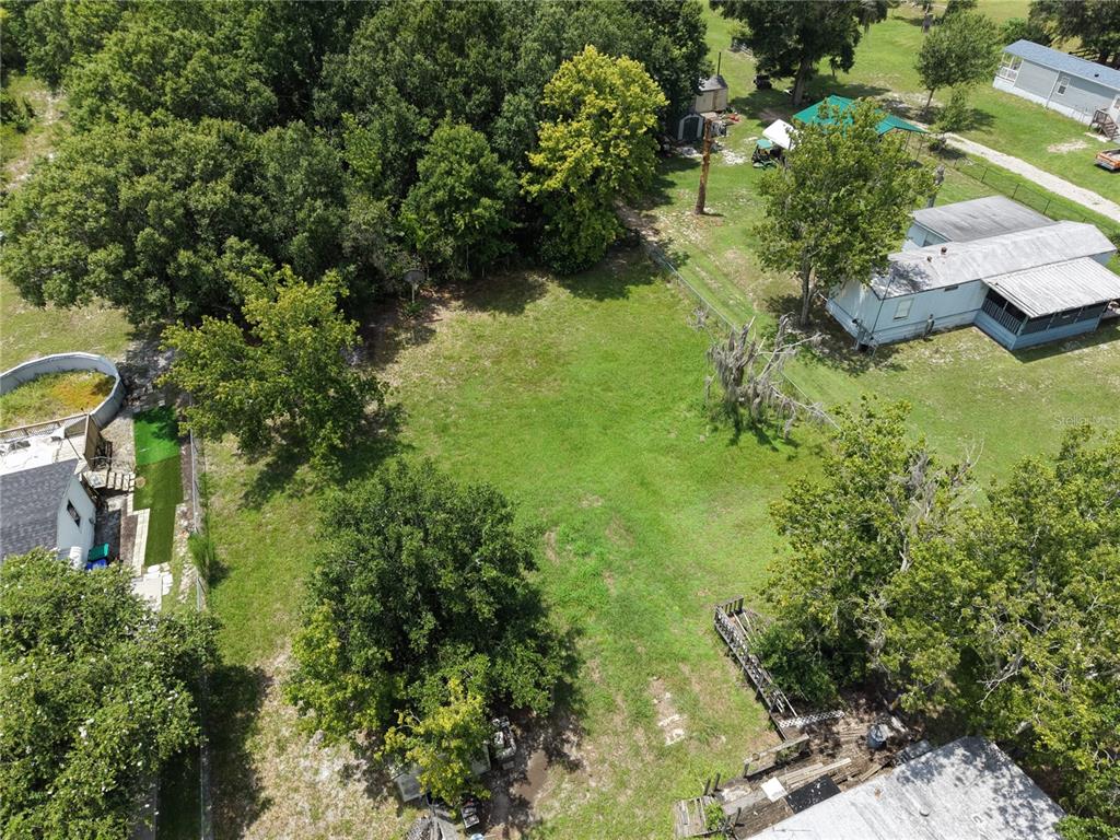 An aerial view shows a grassy lot surrounded by trees and neighboring residential properties — 18440 AMITYVILLE DR, ORLANDO, FL