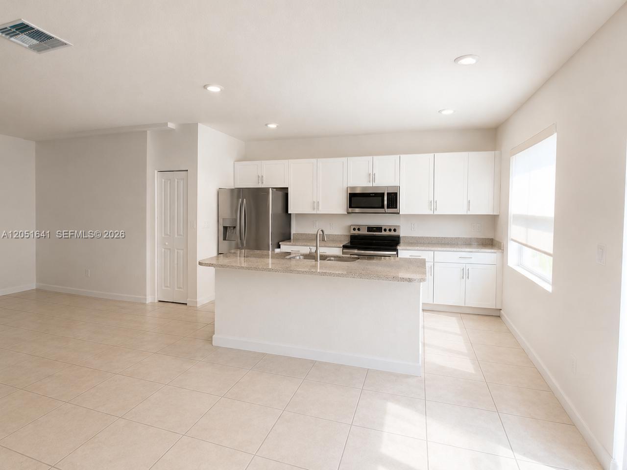 A bright kitchen features white cabinets, stainless steel appliances, and a granite-topped island — 25328 SW 108th Ct, Homestead FL 33032, HOMESTEAD, FL