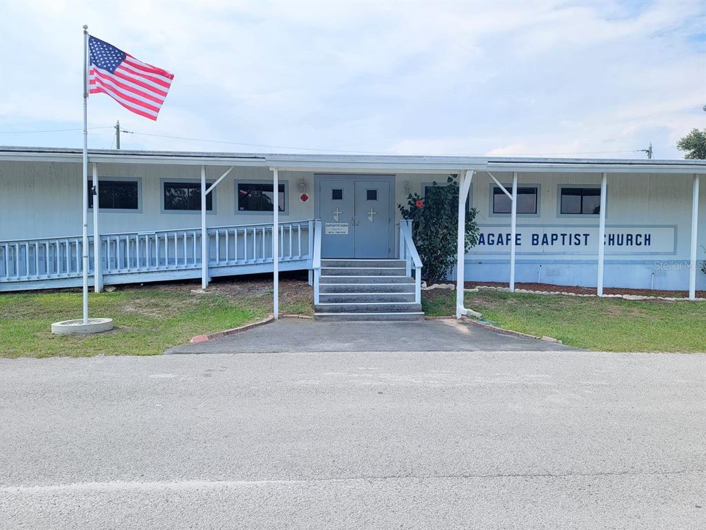 The exterior of a single-story church building features a wheelchair ramp, stairs, and an American flag — 39735 CHANCEY ROAD, ZEPHYRHILLS, FL