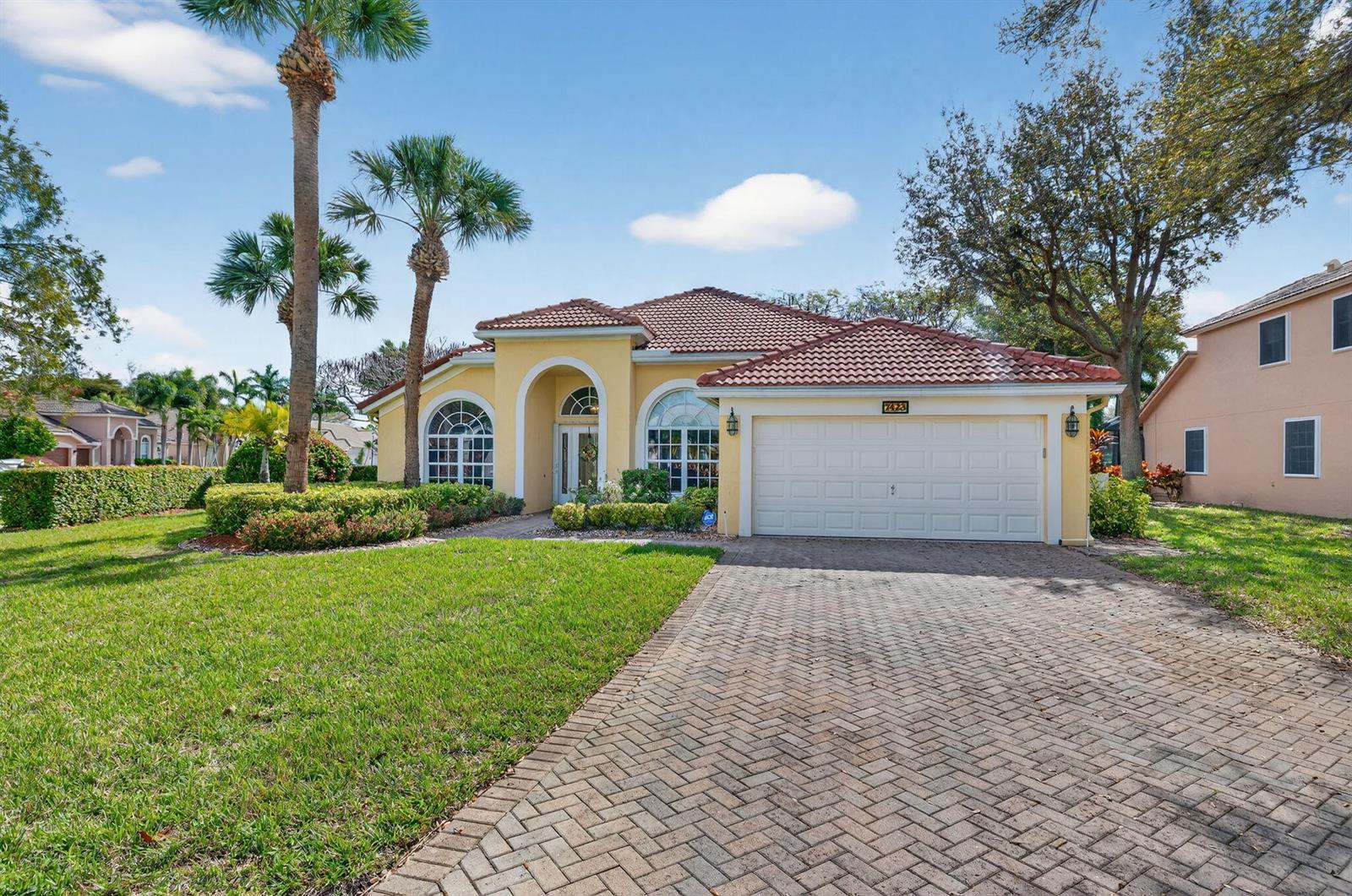 A yellow single-story house with a tile roof, arched windows, and a brick driveway — 7423 Brunswick Circle, Boynton Beach FL 33472, BOYNTON BEACH, FL