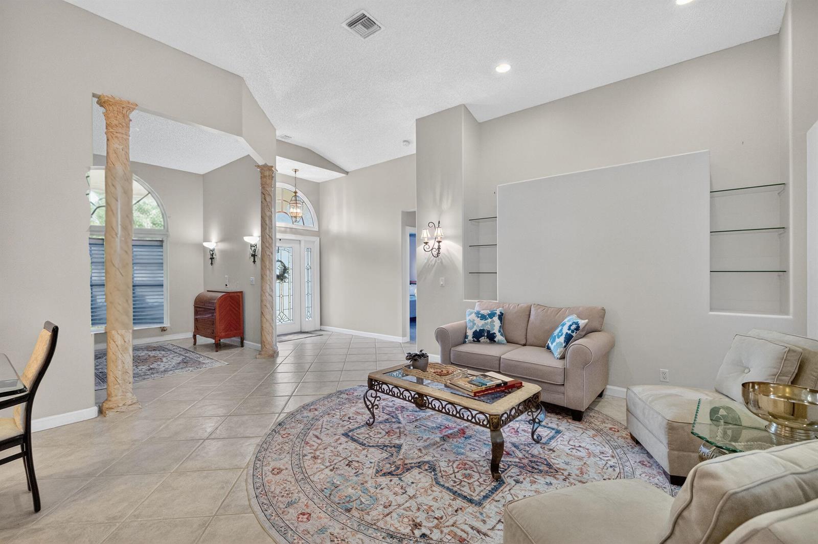 A living room with tile floors, decorative columns, arched windows, and built-in glass shelving — 7423 Brunswick Circle, Boynton Beach FL 33472, BOYNTON BEACH, FL