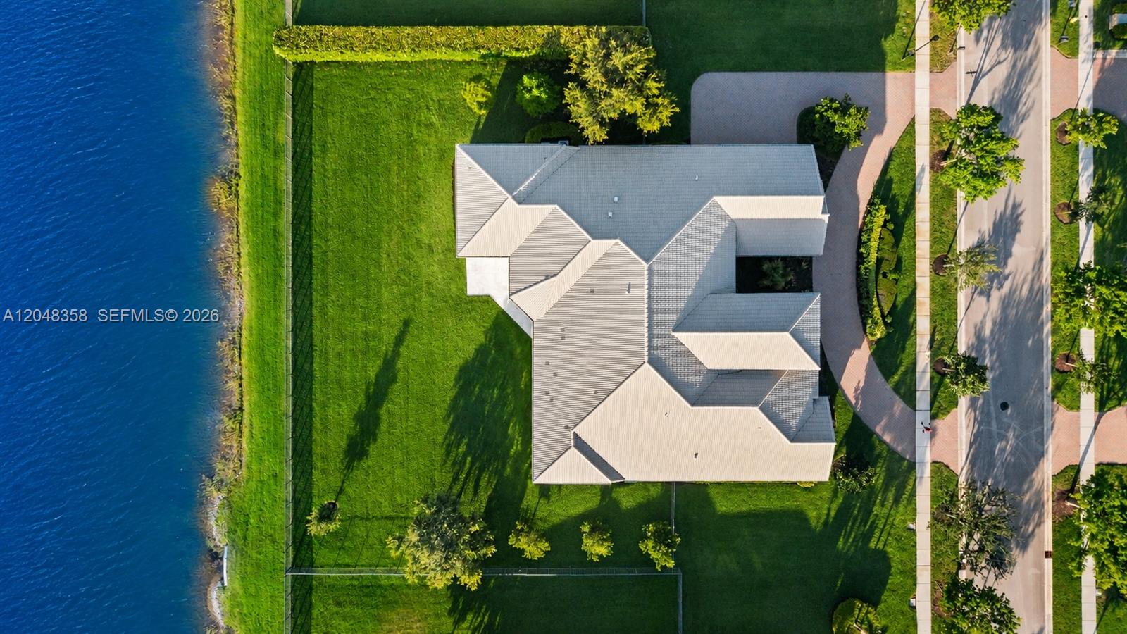 An aerial view shows a house with a light-colored roof situated next to a lake — 5301 S Sterling Ranch Cir, Davie FL 33314, DAVIE, FL