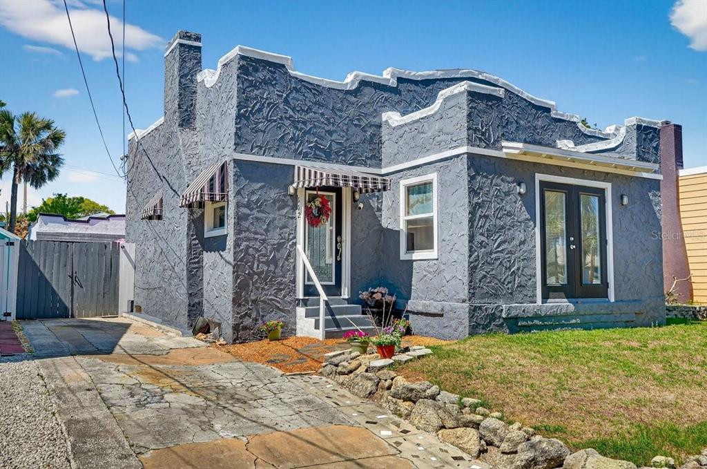 A gray, single-story stucco house with a flat roof, striped awnings, and a concrete driveway — 112 S OLEANDER AVENUE, DAYTONA BEACH, FL