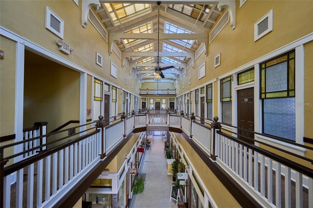 An indoor atrium with a glass ceiling, wooden railings, and multiple doors along the hallway — 230 E PARK AVENUE, LAKE WALES, FL