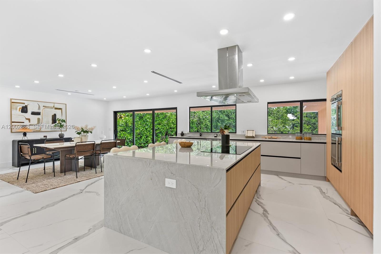 A modern kitchen features a large stone island, light wood cabinetry, and white marble flooring — 19731 NE 24th Ave, Miami FL 33180, MIAMI, FL