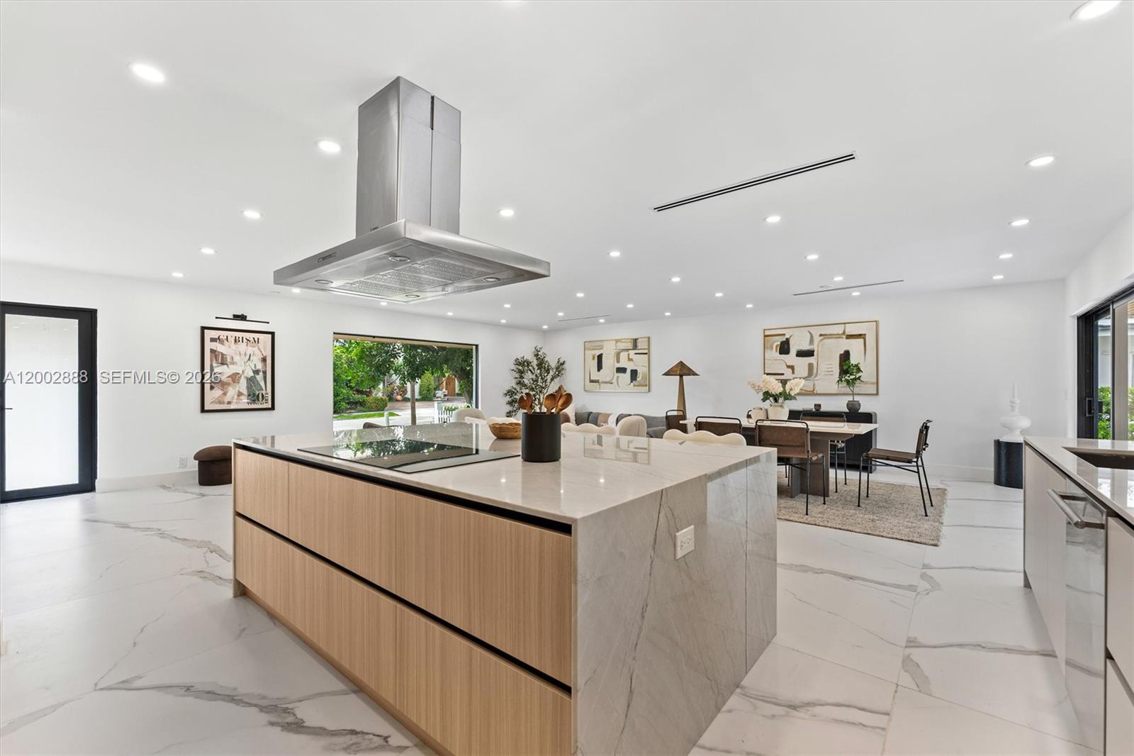 A modern kitchen features a large marble-topped island with wood cabinetry and white tile floors — 19731 NE 24th Ave, Miami FL 33180, MIAMI, FL