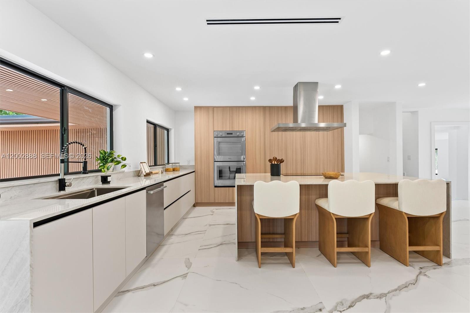 A modern kitchen features light wood cabinetry, a marble-topped island, and white marble flooring — 19731 NE 24th Ave, Miami FL 33180, MIAMI, FL