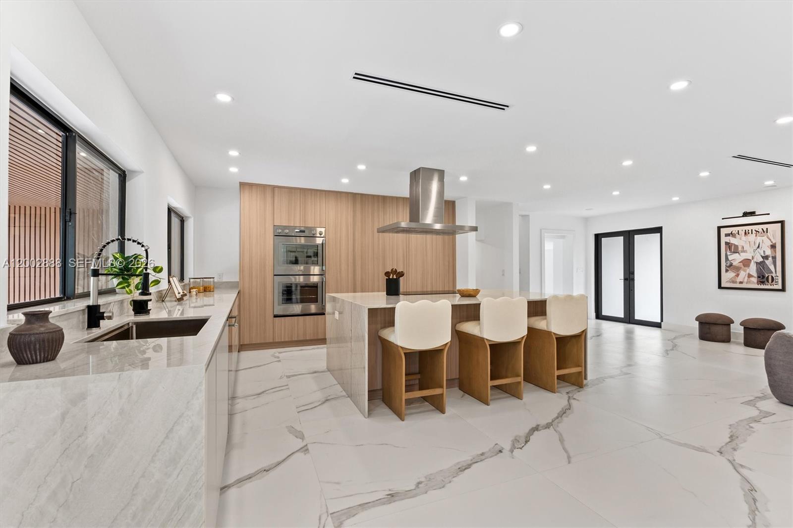 A modern kitchen features light wood cabinetry, a marble island with barstools, and white flooring — 19731 NE 24th Ave, Miami FL 33180, MIAMI, FL